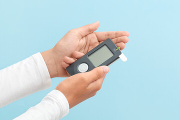 Glucometer in hands on a blue background. Diabetes. Measuring blood sugar levels. Top view. Space for text.