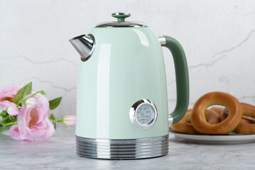 Modern electric kettle on kitchen table with roses and bagels in background.