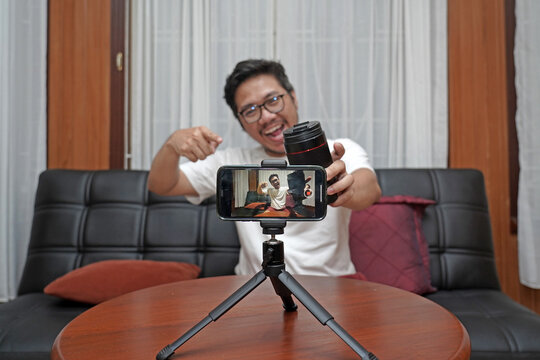 Youtuber talking about photography and a lens while filming with smartphone at home - Powered by Adobe