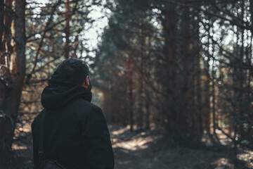 A man in a hood stands on a path in the forest and admires nature. The man enjoys the view of wild...