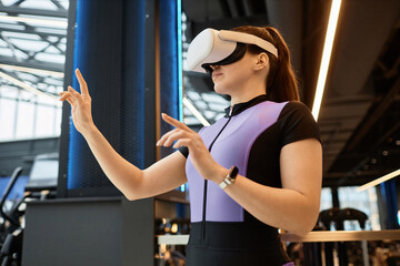 Side view portrait of young sportswoman wearing VR headset in gym and using interactive technology...