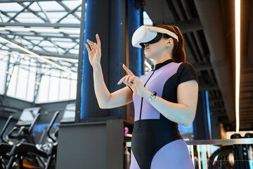 Side view portrait of young sportswoman wearing VR headset in futuristic gym training and using interactive hand tracking copy space
