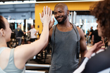 Waist up portrait of smiling Black fitness coach high five with client meeting for training in gym
