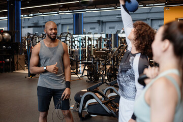 Portrait of muscular African American man as fitness coach watching client in gym giving...