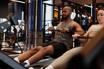 Portrait of muscular Black man using rowing machine during strength training in gym