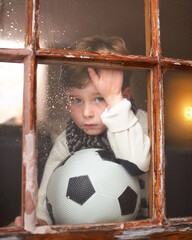 Portrait, depressed and sad child by window with anxiety for bullying trauma, soccer ball and...