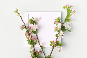 Fresh branches of apple white and pink blossoms and white empty frame on gray table. Mockup for special offers as advertising or other ideas. Empty place for inspirational, motivational text or quote.