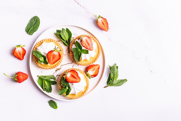 Fresh homemade tart with cream, strawberries and mint leaves on white stone background with copy space for your design top view.
