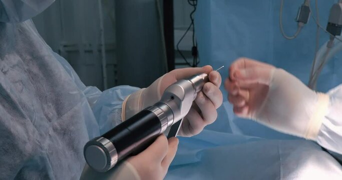 A pin is inserted into an orthopedic drill for osteosynthesis of a bone fracture. A surgeon prepares a surgical drill and pin to fix a bone fracture in the operating room.
