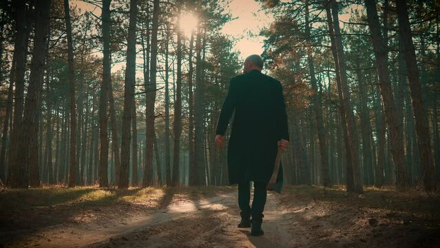 Killer in forest, maniac wearing coat with axe in hands walking between trees in foggy forest, looking around. Bloodthirsty criminal maniac carrying case, searching for victim