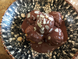 Delicious profiteroles with chocolate and white plate. Selective focus image on light background.