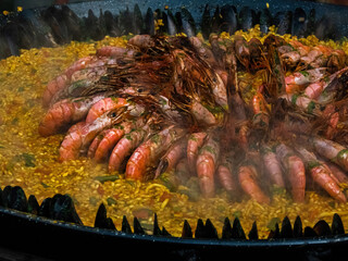 paella with rice, shrimp and shellfish in a large cauldron, street food