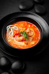 Composition of tom yam soup with shrimp and noodles on black background. The Art of Japanese Cuisine. Food photography for menu and sushi bar decoration 