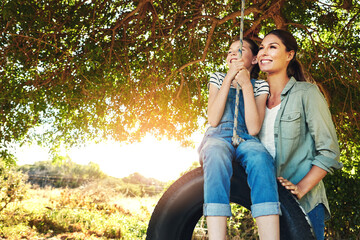 Happy, mother and child on swing outdoor for bonding and play fun game together in nature. Smile, mom and push girl in playground on tire at park for love, care and family holiday on summer vacation