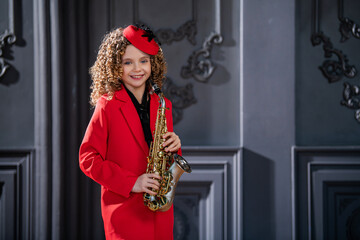 A young girl in a red coat and hat is holding a saxophone.