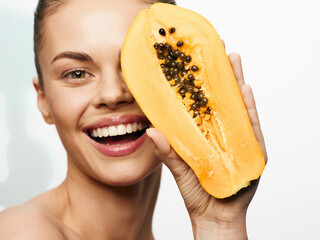 Smiling woman holding papaya in front of face, tropical fruit concept photo shoot with happy model