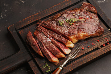 Medium rare sliced grilled striploin beef steak served on wooden board with vintage fork, salt,...