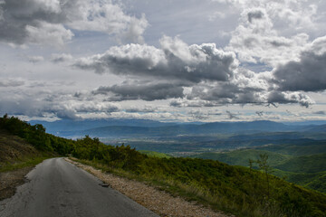 Sunny weather with beautiful and clear clouds in the sky. An asphalt road with many curves leads through the mountain.