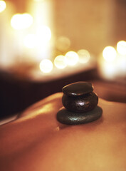 Person, back and hot stone treatment or spa relax at hotel resort or luxury holiday, stress relief or muscle. Client, wellness and tension release or candle bokeh for skincare health, massage or calm