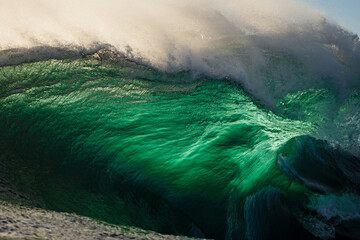 Huge back-lit emerald colored wave breaking over a shallow reef