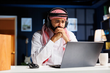 A focused man in traditional Arabic attire works diligently at his desk, utilizing wireless...