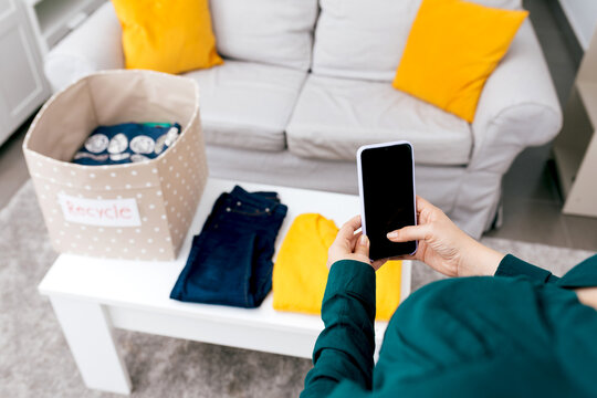 Person using smartphone while organizing recycled clothes