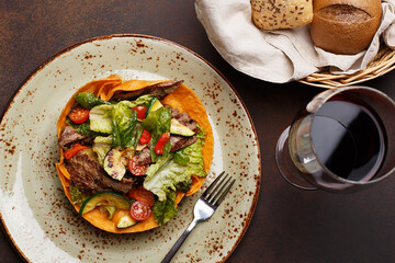 Salad with grilled meat and vegetables in tortillas basket with glass of wine on brown concrete background. Top view
