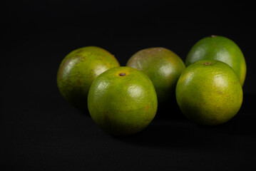 Group of still green oranges on a black background.