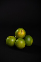 Group of still green oranges on a black background.