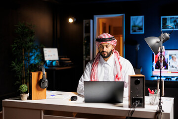 At modern workstation, confident Arab businessman types on his laptop. Muslim guy is browsing,...