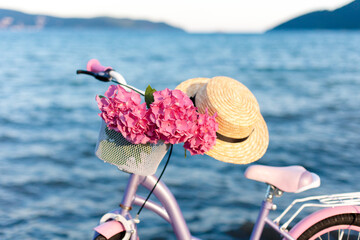 Bike on sea beach. Female romantic bicycle with pink hydrangea flowers in basket, straw sun hat. Riding on coastline. Concept of happy summer holiday and cycling on vacation. Ecological transportation