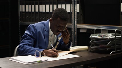 Black policeman conducts confidential investigation, analyzes evidence and makes crucial phone calls. African american law officer uses telephone to collect classifed witness statements and clues.