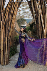 A lady in formal wear and purple saree poses by a wooden archway