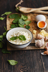 Natural healthy ingredients for cooking - cottage cheese, parmesan cheese, baby spinach leaves, garlic, raw egg and peppercorns on wooden table. Side view, close up