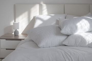 A bed with white pillows and a blanket, next to a bedside table with a lamp, daylight