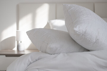 A bed with white pillows and a blanket, next to a bedside table with a lamp, daylight
