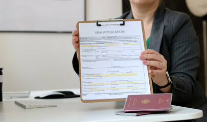 Close up of a woman holding a visa application paper document with a German passport laying on...