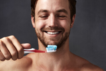 Face, oral hygiene and toothbrush with man in studio isolated on blue background for dental care. Brushing teeth, product and toothpaste with person in bathroom, cleaning mouth for protection