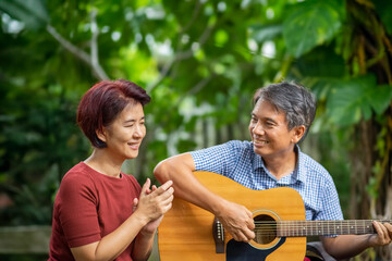 Fototapeta premium Middle aged couple playing guitar while relax sitting on bench in backyard.