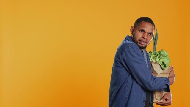 Vegan person acting overprotective of his eco friendly groceries bag, protecting his freshly harvested goods in studio. Serious man taking care of his bio organic belongings. Camera B.