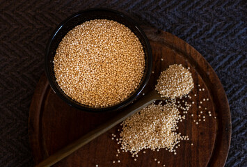 A group of quinoa seeds on wooden spoon and grais of quinoa in black bowl .