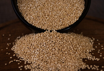 Close-up photo of quinoa grains falling on wooden board. Dark background