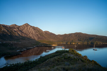 Fototapeta premium World heritage port davey national park in tasmania Australia, with mountains and river. boats in a bay in the evening