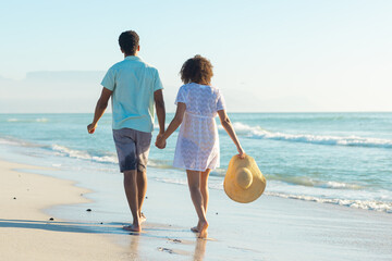 Obraz premium At beach, biracial couple holding hands, walking along shore