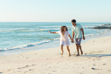 Obraz premium At beach, biracial couple holding hands, walking, both smiling