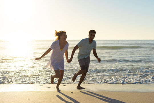 At beach, biracial couple holding hands, running along shore - Powered by Adobe