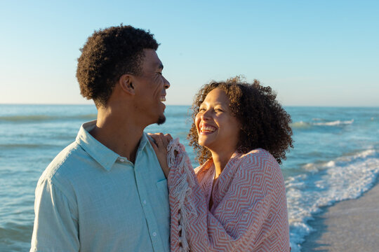 At beach, diverse couple standing, laughing together