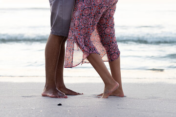 Obraz premium At beach, biracial couple walking barefoot, waves nearby