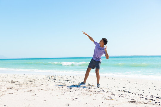 At beach, biracial young man throwing frisbee, wearing purple shirt