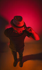 A man wearing a hat and a black shirt stands in front of a red background